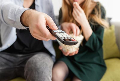 A photo of a couple eating popcorn on a couch with the man holding the remote control