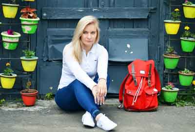 Blonde woman sitting next to a red backpack.