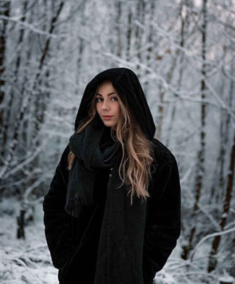 A brunette Russian woman in black standing in a snowy white forest.